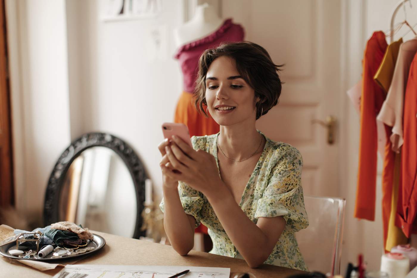 Dueña de pequeño negocio fotografiando productos para Instagram con smartphone en mesa de madera con flores y props